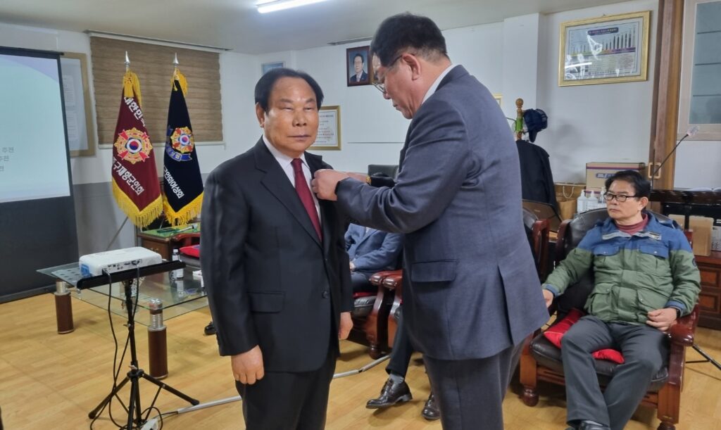 김정일 지회장이 신임 동 회장에게 임명장을 수여하며 왼쪽 가슴에 배지를 달아주고 있는 모습