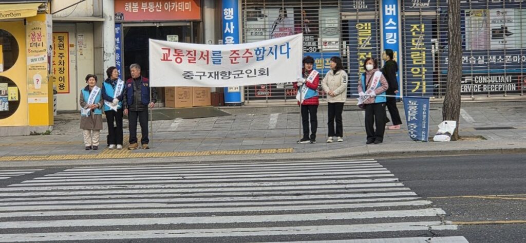 횡단보도 앞에서 시민들을 향해 교통법규 준수 홍보물을 들고 서 있는 봉사자들