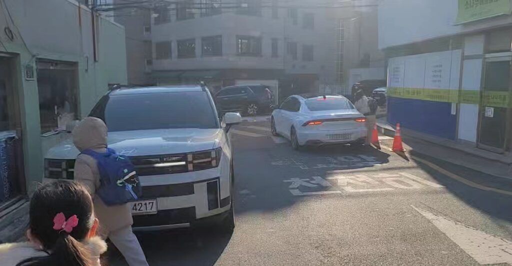 좁은 골목길에 차량들이 엉켜 있는 사이로 가방을 메고 하교 중인 어린이의 위태로운 모습