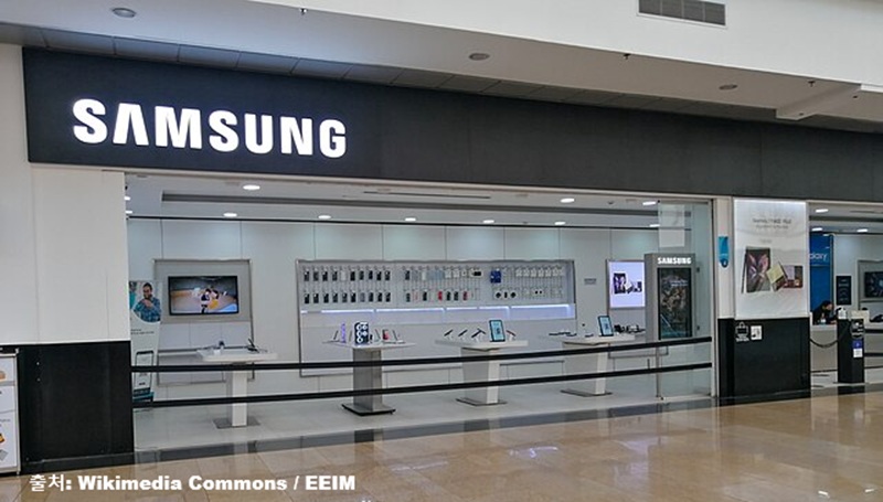 현대적인 쇼핑몰 내부에 입점한 깔끔하고 세련된 삼성(SAMSUNG) 공식 브랜드 스토어의 외관 전경과 삼성전자의 2026년 임금협상 결렬 및 성과급 체계 개편 논란 관련 경제 보도 이미지 (출처: Wikimedia Commons / EEIM)