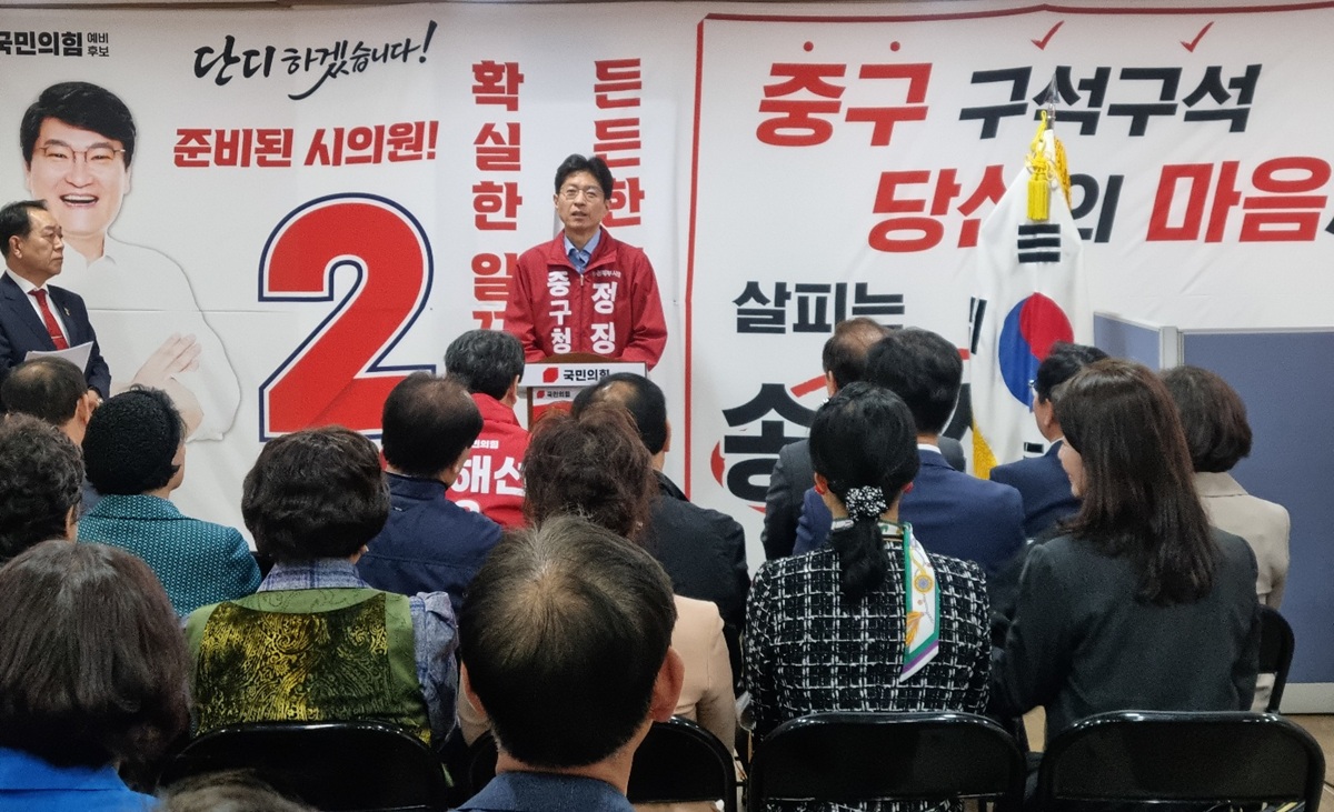 송해선 시의원 후보 개소식에서 정장수 중구청장 후보가 마이크를 잡고 축사를 하고 있는 모습. 뒤편 현수막에는 '준비된 시의원 송해선' 문구가 보이며, 류규하 후보를 비롯한 내빈들이 나란히 앉아 경청하고 있다.